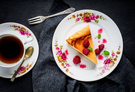Cheesecake slice with raspberries and mint leaves on plate.の写真素材