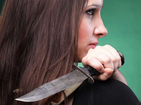 Sexy young woman in red with a gun, knife on green backgroundの写真素材