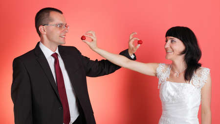 Happy smiling bride and groom young happy couple playfully eating strawbery on red backgroundの写真素材