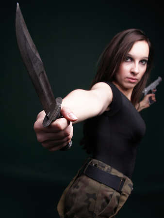 Sexy young woman in red with a gun, knife on green backgroundの写真素材