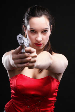 Sexy young woman in red with a gun on black backgroundの写真素材