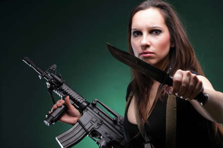 Sexy young woman in red with a gun, knife on green backgroundの写真素材