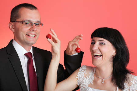 Happy smiling bride and groom young happy couple playfully eating strawbery on red backgroundの写真素材