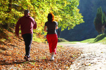 Woman and man walking cross country and trail in autumn forestの写真素材