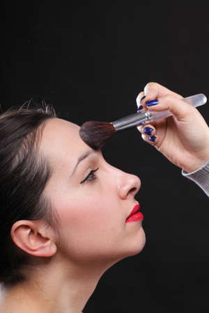 beautiful young brunette woman applying powder with a brush, on black backgroundの写真素材