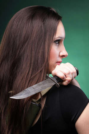 Sexy young woman in red with a gun, knife on green backgroundの写真素材