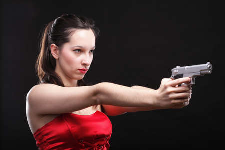 Sexy young woman in red with a gun on black backgroundの写真素材