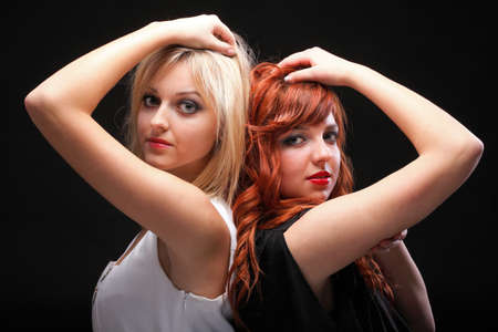 two happy young girlfriends blonde and red-hair black background Glamourの写真素材