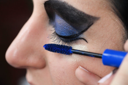 Charming young woman applying blusher eyelid close up blue