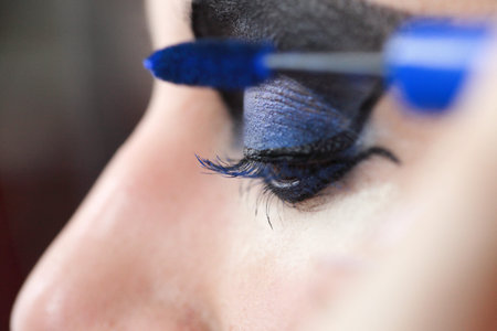 Charming young woman applying blusher eyelid close up blue