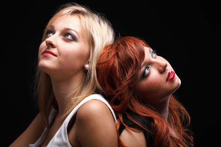 two happy young girlfriends blonde and red-hair black backgroundの写真素材