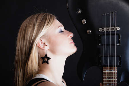 Rock music. Blonde girl guitarist musician performer with electric guitar musical string instrument on black. Concert.の写真素材