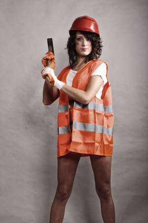 Sex equality and feminism. Sexy girl in safety helmet orange vest holding hammer tool. Attractive woman working as construction worker.の写真素材