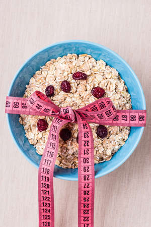 Diet healthy food weight loss concept. Oatmeal in blue bowl with measuring tape around on kitchen tableの写真素材