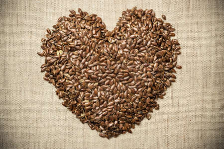 Diet healthcare healthy food. Raw flax seeds linseed heart shaped on sack burlap background.の写真素材