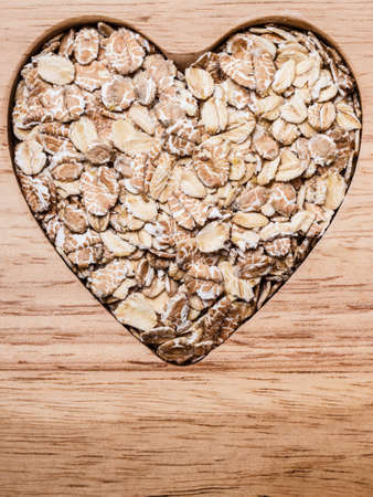 Dieting healthcare concept. Oat cereal oatmeal heart shaped on wooden surface. Healthy food for lowering cholesterol.の写真素材