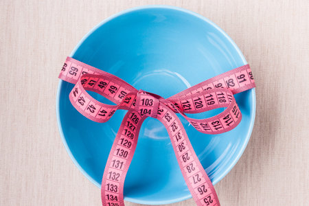 Dieting healthy lifestyle and slim body concept. Pink measuring tape around empty blue bowl on...