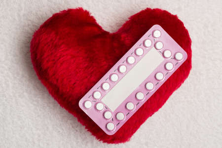 Medicine contraception love and birth control. Oral contraceptive pills on red heart shaped little pillowの写真素材