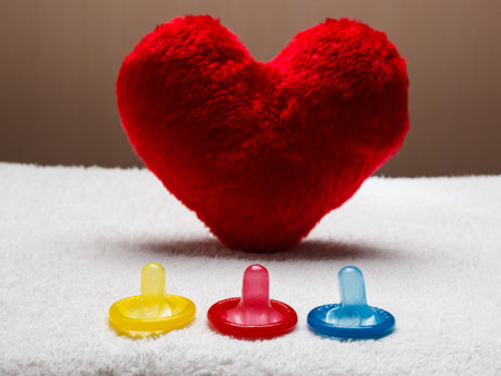 contraception love and birth control. Colorful condoms and red heart shaped little pillow