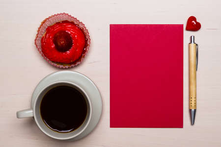 Coffee cup sweet cake cupcake and red paper blank with pen on wooden surface, top view copy space for textの写真素材