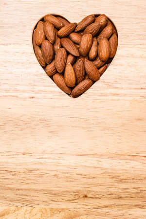 Whole food, good for health. Heart shaped almonds on wooden surface board backgroundの写真素材