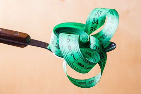 Diet food healthy lifestyle and slim body concept. Closeup green measuring tape centimeter on kitchen spoonの写真素材