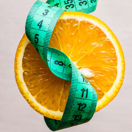 Diet healthy eating and slim body concept. Closeup green measuring tape centimeter and orange fruitの写真素材