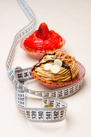 Appetite and gluttony concept. Fattening problem. Cakes cupcakes with measuring tape on tableの写真素材