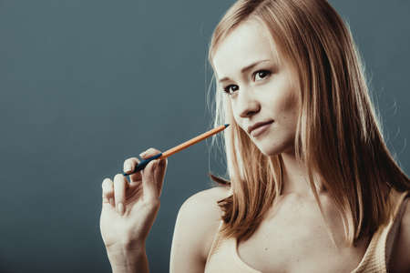 Thoughtful woman face. Attractive blonde girl holding a pen thinking on gray backgroundの写真素材