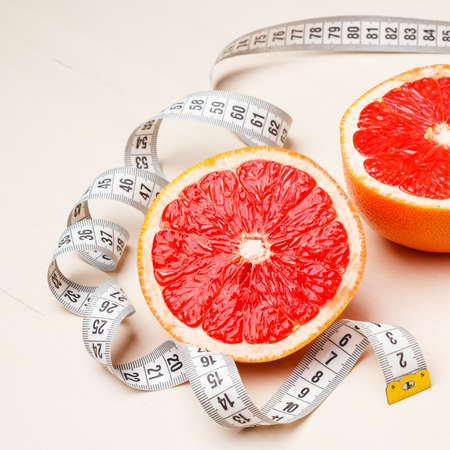 Dieting concept. Closeup grapefruit fruit with measuring tape on tableの写真素材