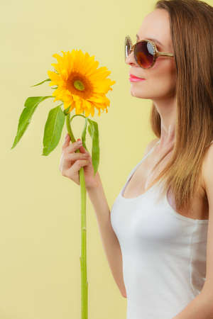 Closeup side view of attractive summer woman in sunglasses with sunflower in her hand on yellow backgroundの写真素材