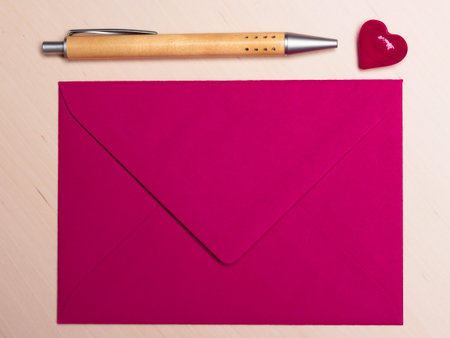 Pink blank envelope little heart and pen on wooden surface. Valentine day card, love or wedding greeting concept.の写真素材