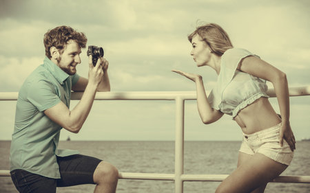 Young couple in love is taking photos on sea pier. Boyfriend photographing his lovely girlfriend outdoor on sea pierの写真素材