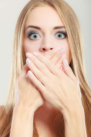 Closeup young amazed woman wide eyed covering her mouth with hands on grayの写真素材
