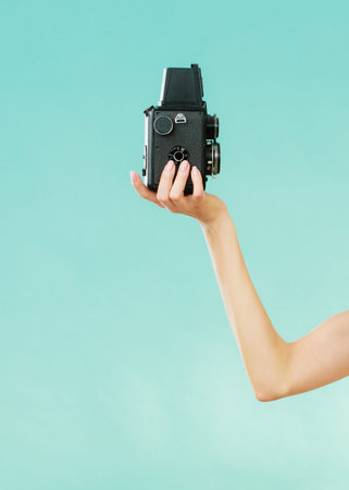 Female hand holding old vintage camera, woman taking self picture vivid blue background