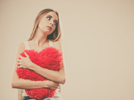 Broken heart love concept. Sad unhappy woman hugging red heart pillow closeupの写真素材