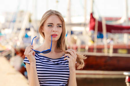 Travel tourism and people concept. Fashion blonde girl with blue heart shaped sunglasses in marina against yachts in portの写真素材