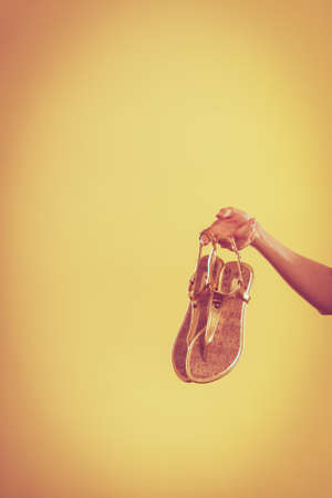 Holidays summer fashion concept. Woman holding golden sandals in hand bright background copy spaceの写真素材