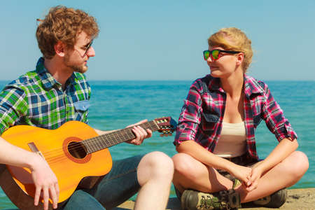 Young man playing guitar to his girlfriend outdoor by seaside - dating coupleの写真素材