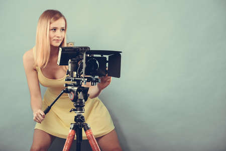 Photographer girl shooting images. Attractive fashionable blonde woman taking photos with camera blue backgroundの写真素材