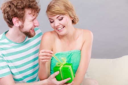 Couple sitting on couch at home. Young man giving woman gift boxの写真素材