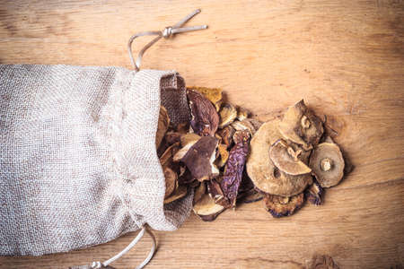 Food. Closeup dry mushrooms spilling out from burlap sack on wooden surface table background.の写真素材