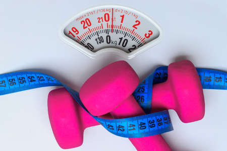 healthy lifestyle fitness weight control concept. Closeup pink dumbbells with blue measuring tape on white scalesの写真素材