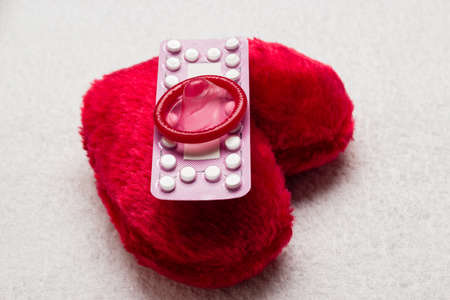 Medicine contraception love and birth control. Oral contraceptive pills condom on red heart shaped little pillowの写真素材