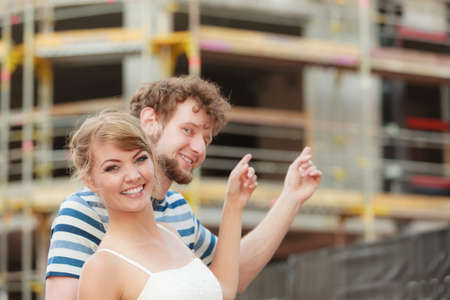 Real estate and family concept - young couple on front of new big modern house dreaming about home showing with fingersの写真素材