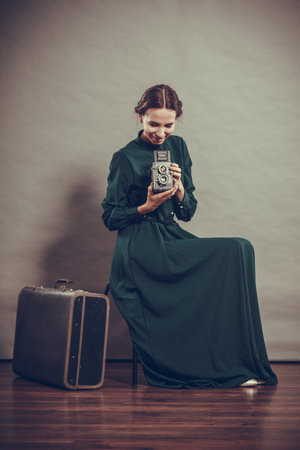 Woman retro style long dark green gown old suitcase and camera, taking picture vintage photoの写真素材