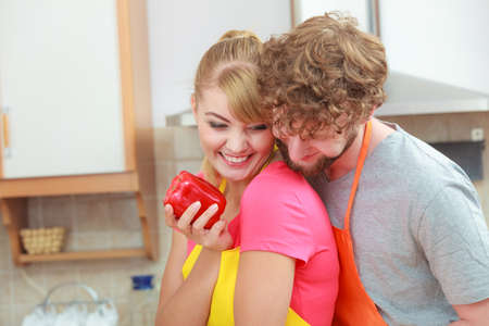 Happy young couple cooking. Woman and man having fun in kitchen at home preparing fresh vegetables food salad. Girl holds red  pepper in handの写真素材