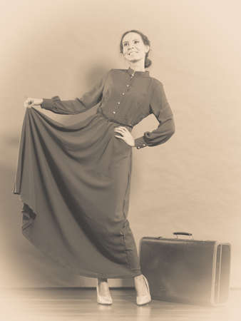 Woman retro style long dark gown with old suitcase, vintage photo sepia tonedの写真素材