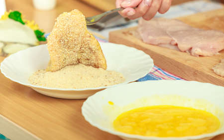 Cooking. Female hand preparing meal of breaded chicken cutlets, rolled raw chops in breadcrumbsの写真素材
