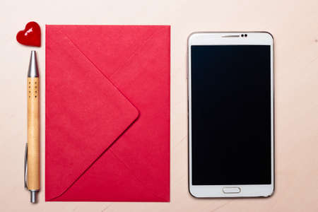 Red envelope little heart, pen and smart phone on wooden surface.の写真素材